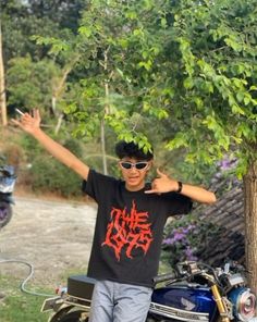 a young man standing next to a motorcycle with his arms in the air and one hand up