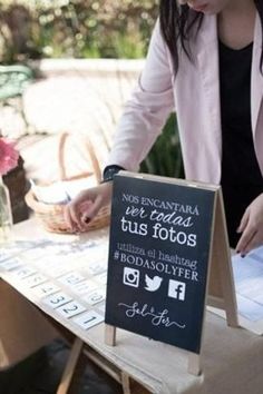 a woman standing at a table with a sign in front of her and writing on it