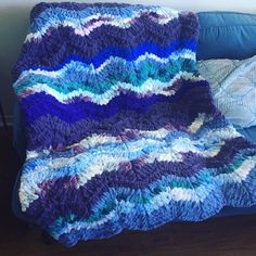 a crocheted blanket sitting on top of a blue couch next to a pillow