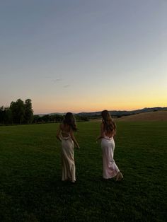 two women are walking in the grass at sunset