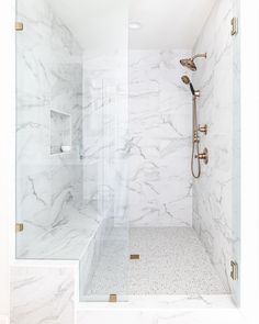 a walk in shower sitting next to a white tiled wall and floor covered in marble