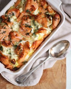 a casserole dish with salmon, cheese and spinach in it on a wooden table