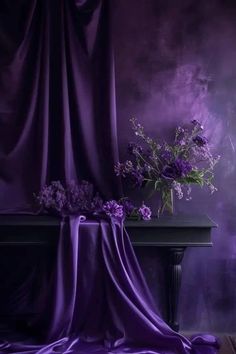 a vase filled with purple flowers sitting on top of a table next to a curtain