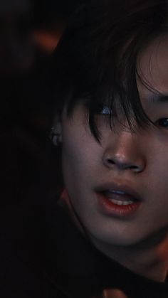 a close up of a person with dark hair and piercings on their ears looking at the camera