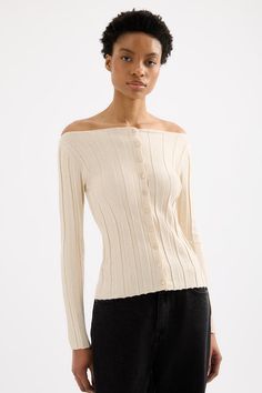 a woman wearing a white sweater and black pants with an off the shoulder button up