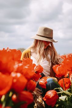 a woman sitting in a field of red tulips wearing a hat and looking at the camera