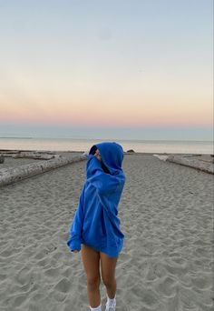 a person wearing a blue robe and white socks standing on the beach at sunset with their back to the camera