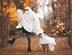 a woman dressed in white is holding on to her dog's leash as they walk through the woods