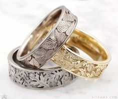 three wedding rings with leaves on them sitting next to each other in front of a white background