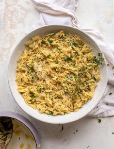 a white bowl filled with pasta and parsley on top of a marble countertop