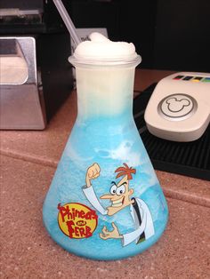 a glass beaker with cartoon characters on it sitting on a counter next to a remote control