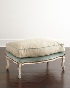 a white ottoman sitting on top of a hard wood floor next to a white wall