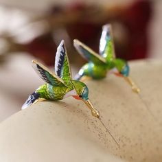 two green birds are sitting on the back of a white pillow with pins in it's wings