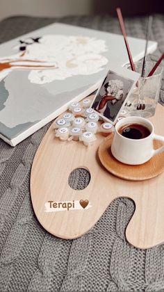 a cup of coffee sitting on top of a wooden tray next to an album and pencils