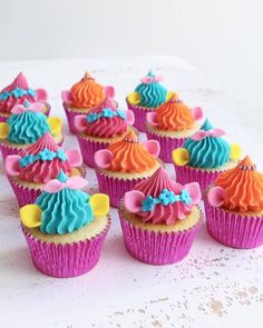 cupcakes decorated with colorful frosting and bows on top of a white table