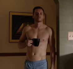 a shirtless man holding a coffee cup in his hand and looking at the camera