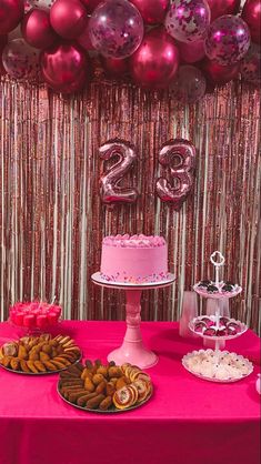 a pink table topped with a cake covered in frosting next to lots of balloons