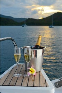 two glasses of wine are sitting on the deck of a boat with a bottle of champagne in it