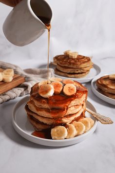 pancakes with bananas and syrup being poured onto them by a person pouring maple syrup on top