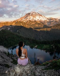 a woman sitting on top of a rock next to a lake in the middle of mountains