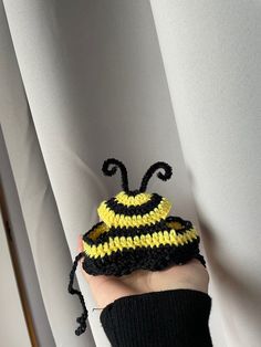 a hand is holding a crocheted hat with a yellow and black bee on it