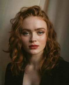 a woman with red hair and blue eyes is looking at the camera while wearing a black jacket