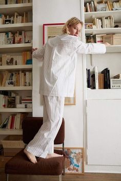 a woman in pajamas is standing on a chair and leaning against a book shelf with books behind her