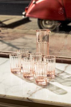 the glasses are lined up on the table by the window sill, and one is empty