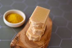 a wooden spoon with some soap on top of it next to a bowl of yellow liquid