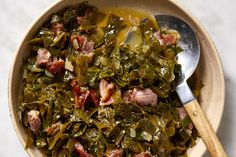 a bowl filled with meat and greens on top of a white countertop next to a wooden spoon