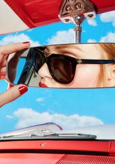 a woman wearing sunglasses looking at her reflection in the side mirror of a red car