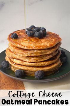 a stack of pancakes on a plate with blueberries and syrup being drizzled over them