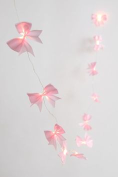 some pink paper flowers are hanging from a string on a white wall with light strings