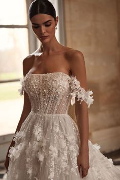 a woman in a white wedding dress with flowers on the skirt and off - shoulder