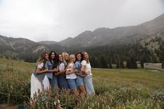 a group of women standing next to each other in a field with mountains in the background