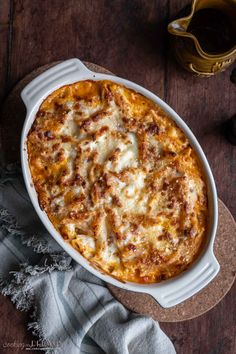 a casserole dish with cheese and sauce in it on a wooden table next to a cup of coffee