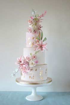 a three tiered wedding cake with pink flowers and gold leaf decorations on it's side