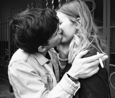 black and white photograph of two people kissing each other in front of an iron gate