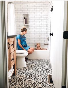 a woman and child sitting in a bathtub with black and white tiles on the floor