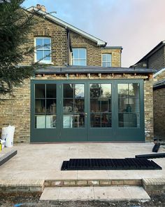 a house with green doors and windows next to a stone walkway in front of it