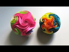 two colorful balls sitting next to each other on top of a white table with one being made out of paper