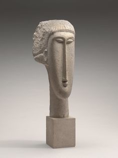 a white sculpture with a face on it's head and one eye open, in front of a gray background