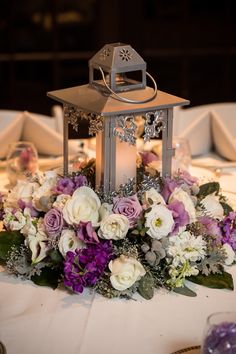 a table topped with a lantern and flowers on top of a white table cloth covered table