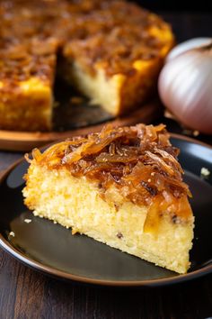 a piece of cake sitting on top of a black plate next to a garlic and onion dish