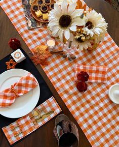 an orange and white checkered table cloth with flowers on it is set for a thanksgiving dinner