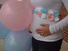 a pregnant woman standing next to balloons in front of a brick wall with flowers on it