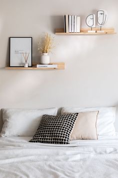 a bed with white sheets, pillows and two shelves on the wall above it that are filled with books