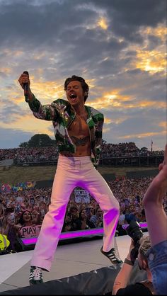 a man standing on top of a stage with his arms in the air while people watch