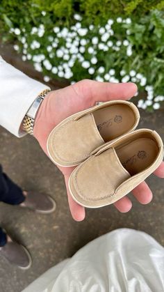 a person holding two pairs of shoes in their hand while standing next to some flowers