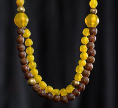 A double-strand necklace made of recycled Krobo glass made by Artisans in Ghana, old yellow "tomato" trade beads from Ethiopia, accented with tribal globe brass beads from Nigeria. The necklace is 23" long. The brass an Krobo beads are approximately 14mm in diameter. The two large "connector" beads are 24 mm, the yellow tomato beads are about 12x15mm,=. Tomato beads have some patina on them, showing off their old age. The Krobo and brass beads are not as old, but are made to look antique, and be Handmade Yellow Double Strand Jewelry, Handmade Double Strand Yellow Necklace, Handmade Yellow Double Strand Necklace, Bohemian Yellow Glass Necklace, Artisan Yellow Beaded Necklace With Wooden Beads, Unique Yellow Wooden Beads, Yellow Wooden Beads, Artisan Yellow Wooden Beads, Handmade Yellow Czech Glass Beaded Necklaces